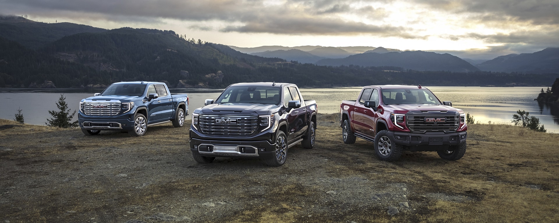 Three GMC trucks parked in front of a mountain lake